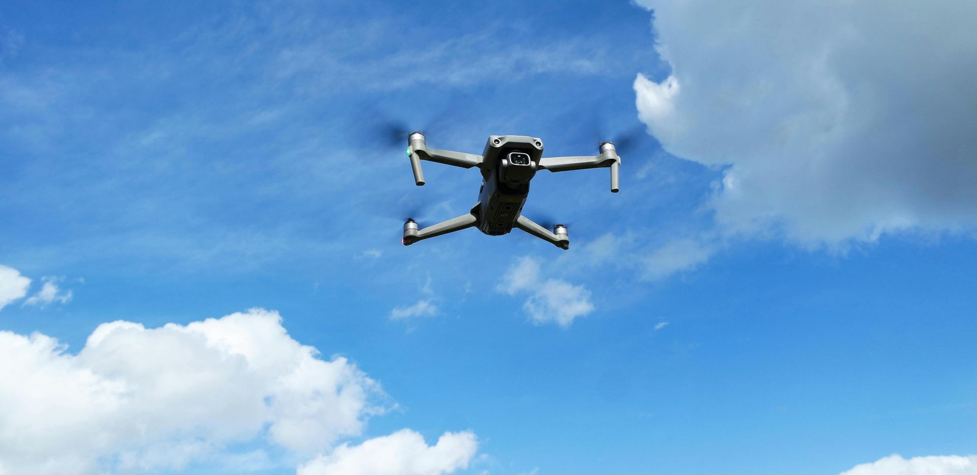 Captivating aerial shot of a drone soaring high in the blue sky with fluffy white clouds.